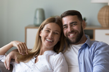 Happy handsome husband and beautiful wife head shot home portrait. Joyful attractive family married couple looking at camera with toothy smiles, laughing, talking on video call