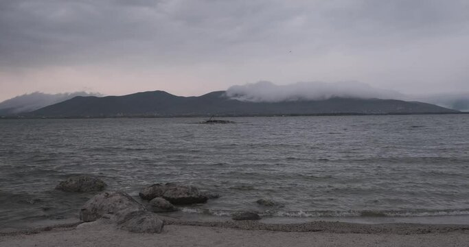 The tranquility of Lake Sevan is evident in this image, where the vast expanse of water meets the sky. The dynamic movement of low-lying clouds adds a sense of motion, making the scene both peaceful