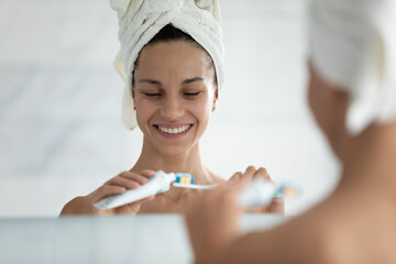 Happy girl in head towel after shower put toothpaste on toothbrush, clean teeth for healthy white...