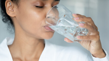 Close up of african American young woman feel thirsty drink clear pure mineral water from glass,...