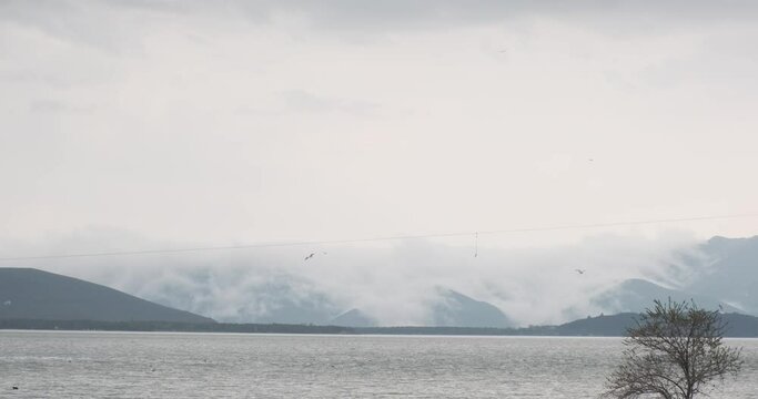 Drifting clouds cast their reflection on Lake Sevan's calm waters. The lake, a jewel of Armenia, offers a view that is both serene and dramatic, especially with the play of light and shadow on its