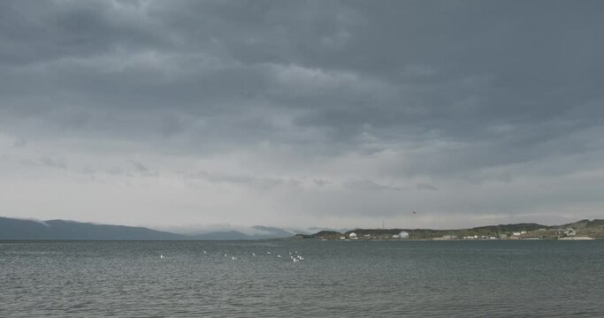 The moody atmosphere of Lake Sevan is palpable as clouds hover just above the water, casting fleeting reflections. The lake, surrounded by Armenia's rugged terrain, offers a breathtaking view