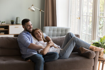 Happy joyful dating couple relaxing in living room together, resting, hugging on sofa, talking,...