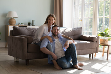 Happy cheerful millennial married couple enjoying being at cozy stylish home, sitting on couch,...