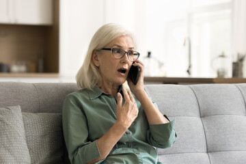 Shocked surprised blonde senior woman excited with telephone call talking on cellphone, speaking emotionally, listening with open mouth, getting awesome news from conversation - obrazy, fototapety, plakaty