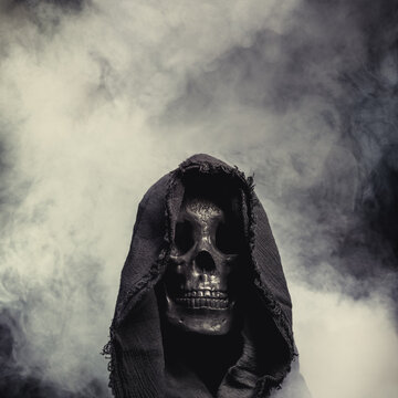 Hooded Grim Reaper figure emerging from the fog. Terrifying human skull, haunted spirt, or frightening ghost rising from dead.