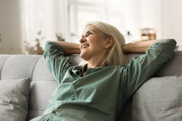 Happy attractive blonde senior woman relaxing on comfortable cozy sofa, leaning on soft back,...