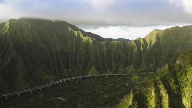 Famous mountain road with jungle nature landscape at sunrise. Scenic aerial with transportation background, travel summer trip 4K. Epic view on H-3 interstate running by cinematic Hawaii island Oahu