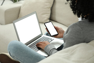 Woman using phone and laptop on sofa indoors, closeup. Space for text