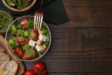 Delicious salad with pesto sauce in bowl, ingredients and fork on wooden table, flat lay. Space for text
