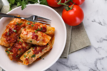 Delicious stuffed cabbage rolls cooked with homemade tomato sauce on white marble table, flat lay