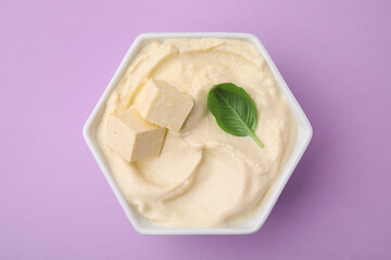 Delicious tofu sauce and basil leaf in bowl on violet background, top view