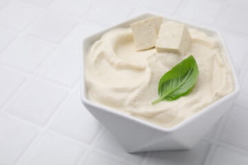 Delicious tofu sauce and basil leaf in bowl on white tiled table, closeup. Space for text