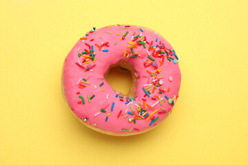 Glazed donut decorated with sprinkles on yellow background, top view. Tasty confectionery