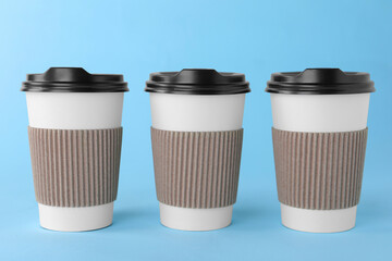 Paper cups with black lids on light blue background. Coffee to go