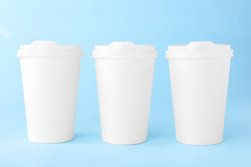 Paper cups with white lids on light blue background. Coffee to go
