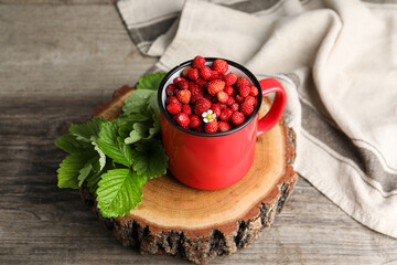 Fresh wild strawberries in mug and leaves on wooden table