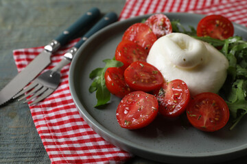 Delicious burrata cheese with tomatoes and arugula served on grey wooden table, closeup