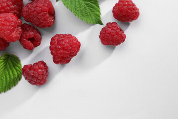 Tasty ripe raspberries and green leaves on white background, flat lay. Space for text