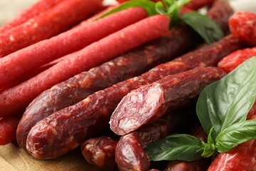 Different thin dry smoked sausages and basil on wooden table, closeup