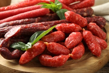 Different thin dry smoked sausages and basil on wooden board, closeup