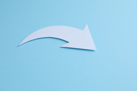 White curved paper arrow on light blue background, space for text