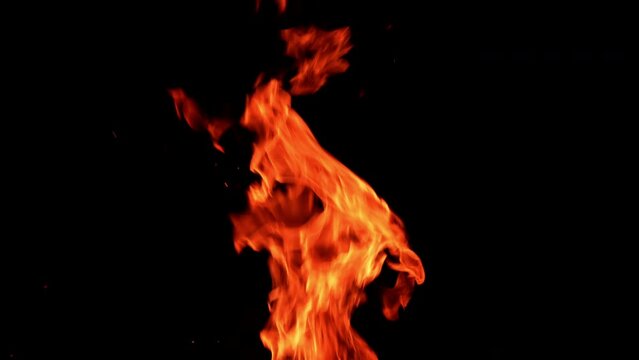 Thin narrow flame burning. Fire going up at the black backdrop. Orange spots flying up.