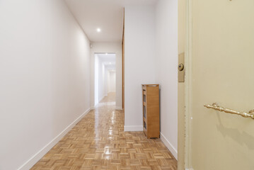 Entrance hall of a house with armored cream-colored wooden door with large golden metal handle, freshly painted smooth white walls and slatted parquet floors