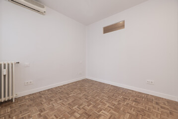 Living room of an empty house with slatted parquet flooring, cast iron radiator and skylight high on the wall
