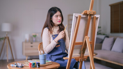 Young asian female artist holding pencil to measuring proportion on the canvas for painting artwork