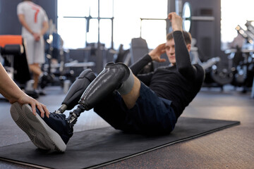 motivated strong man with legs prosthesis doing abdominal crunches, disabled man working out at gym. full length side view shot doing ABS, focus on artificial legs, strength training