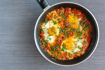 Homemade shakshuka, fried eggs, onion, bell pepper, tomatoes and parsley in a pan. 