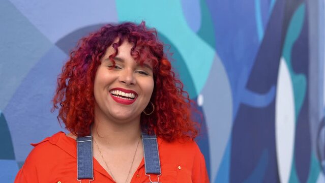 Happy brazilian femele with colour hair against blue wall, looking directly in camera. Body positive