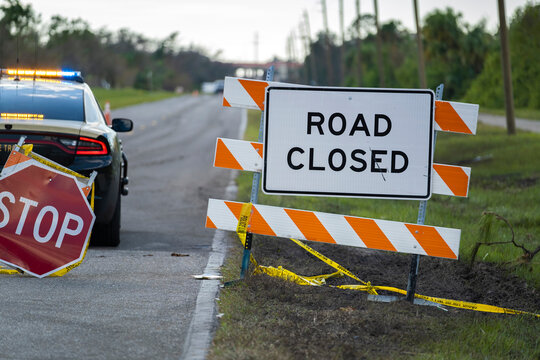 Police patrol car at warning roadworks sign and safety barrier on city street during maintenance repair work