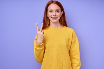 beautiful redhead happy cheerful girl, teacher showing letter V on blue background. Sign language alphabet. free education for deaf children, girl with long red hair showing demonstrating two fingers