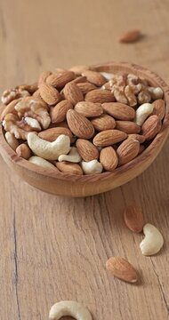 Assorted nuts of almonds, cashews, and walnuts in a wooden bowl. Healthy nutrition concept. Vertical video.
