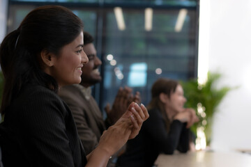 A woman is smiling and clapping with two other people in a room. Scene is positive and celebratory