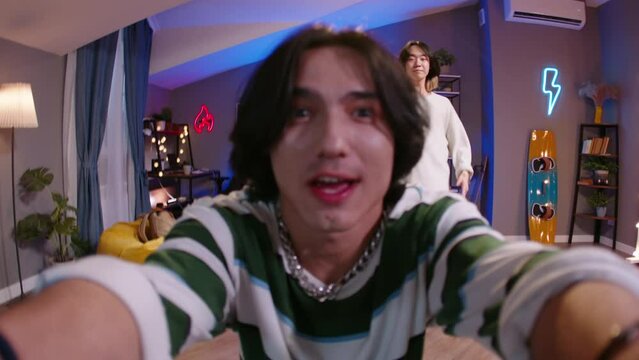 Two Asian Gen Z friends, K-pop dancers, are making trending videos, face close-up. Content creators in cringe happy mood shoot video with k-pop dance posing in colorful neon illumination at home