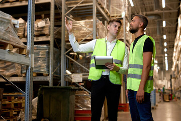 Caucasian two engineers in uniform, checking goods and supplies on shelves in warehouse. logistic and business export. Concept of good management system to support working with industrial business.