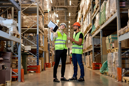 young Caucasian workers in uniform make an inventory management of products on shelves in warehouse, discuss together. Concept of good management system to support working with industrial business.