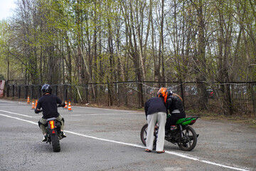 Obraz premium A young woman is learning to ride a motorbike in a motorcycle school. She is taught by a teacher