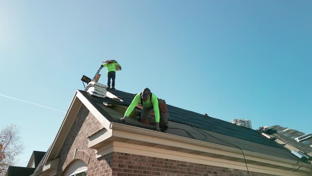 Roofer repair or replace shingle that has been damaged and needing replacement at sunny day. Wide shot. Naperville IL. USA. October 28 2022