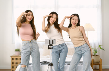 Cheerful Asian women dancing together to music while recording a short video on mobile phone for social media in bedroom at home. Imagination, creativity, Internet technology. influencer Live video