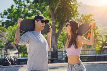 Young happy couple with skateboards enjoy longboarding at the skatepark