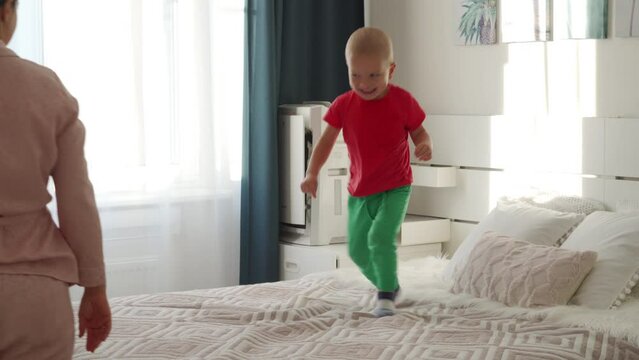 happy child little boy jumping and playing on bed in parents bedroom