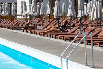 A girl in a black swimsuit rests on a sun lounger by the pool