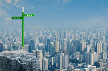 2024 and 2023 direction sign plate with green pencil on rock mountain over modern city tower,...