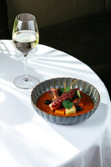 grilled octopus with tomato sauce and vegetables. a glass of whi