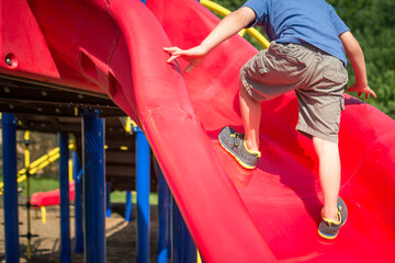 Young boy climbing up slide in suburban playground.