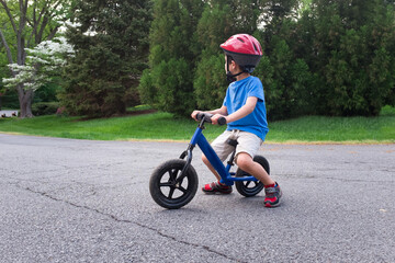 Young boy riding blue balance bike on suburban street.